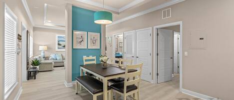 A dining area with a wooden table and chairs, a teal accent wall, and a ceiling light fixture.