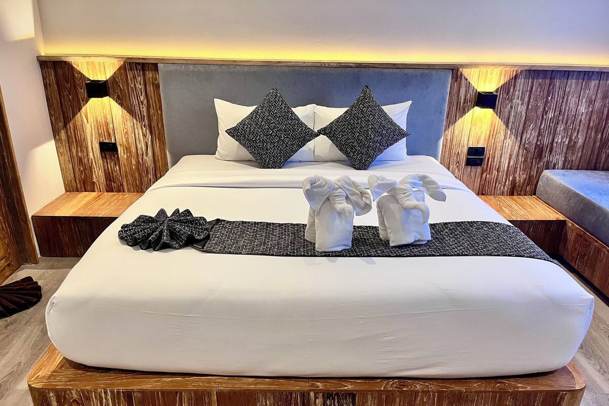 A hotel room with a large bed, wooden headboard, two nightstands, and a wooden bench.