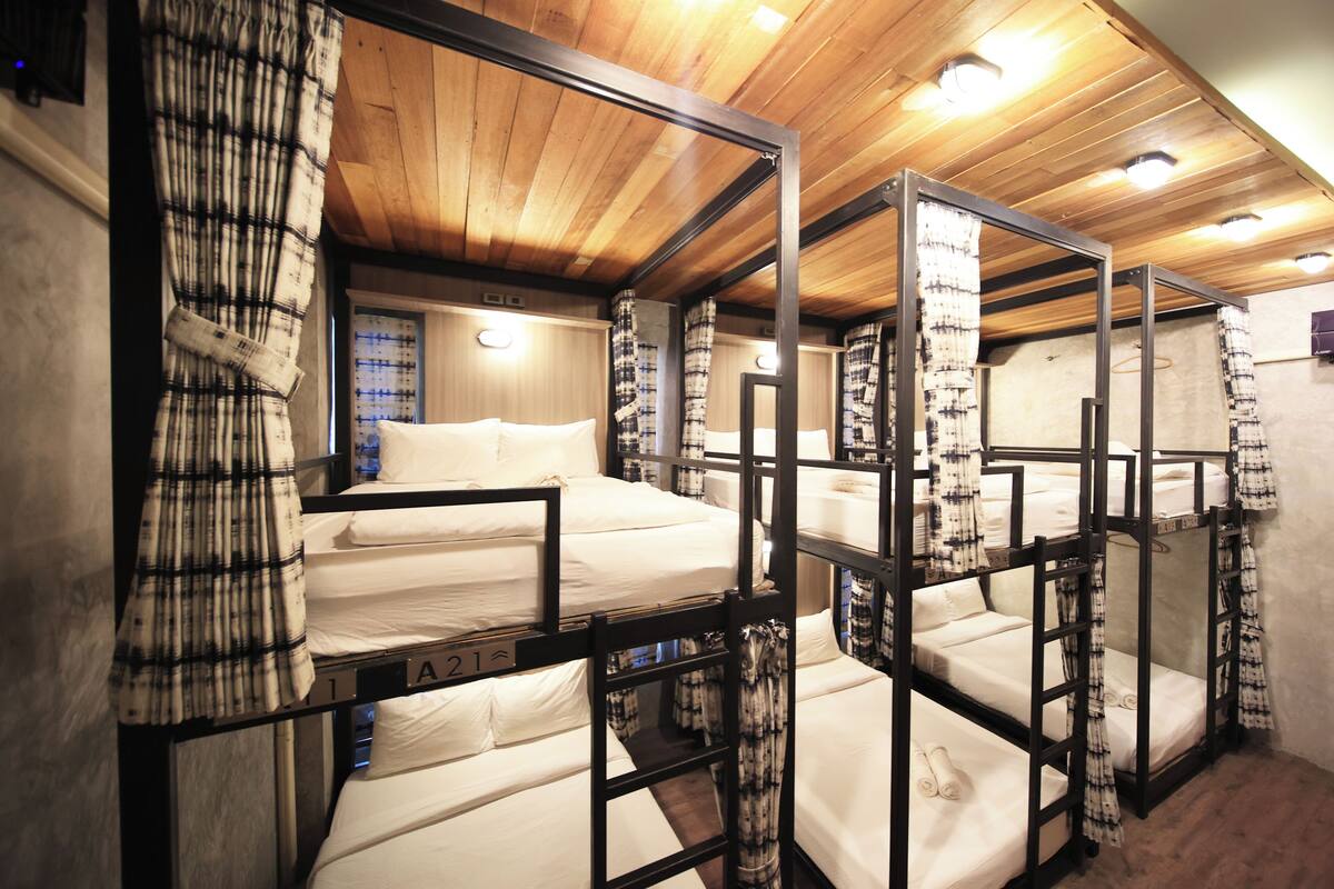 A room with bunk beds, wooden ceilings, and curtains.