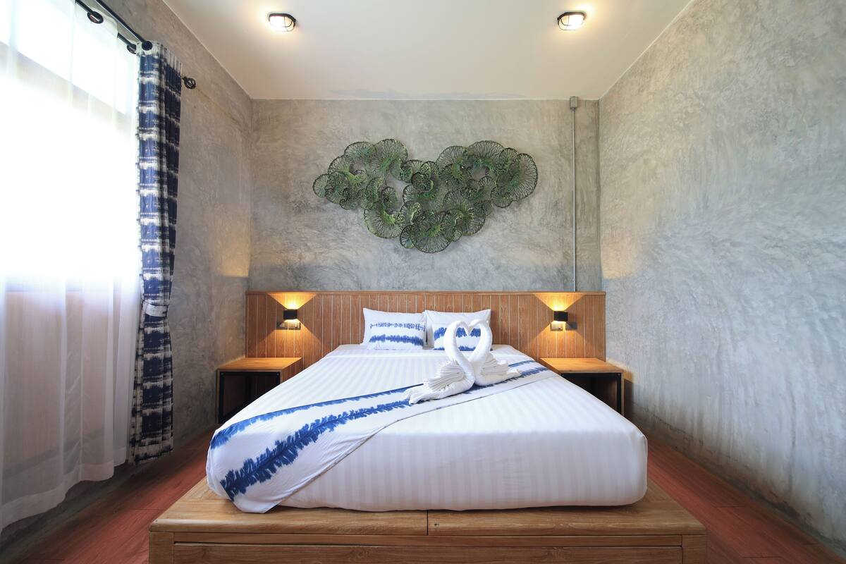A neatly made bed with a blue and white striped blanket, two bedside lamps, and a heart-shaped wall decoration.