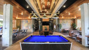 A billiards table in the center of a room with wooden walls and ceiling, surrounded by seating areas and a bar. - The Chic Lipe - Hostel (Koh Lipe)
