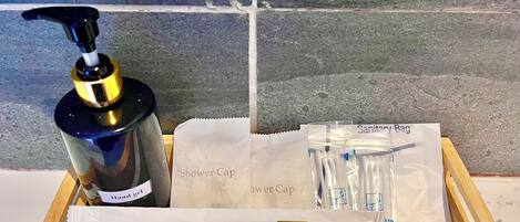 A wooden box containing a shower cap, hand gel, and sanitary bags.