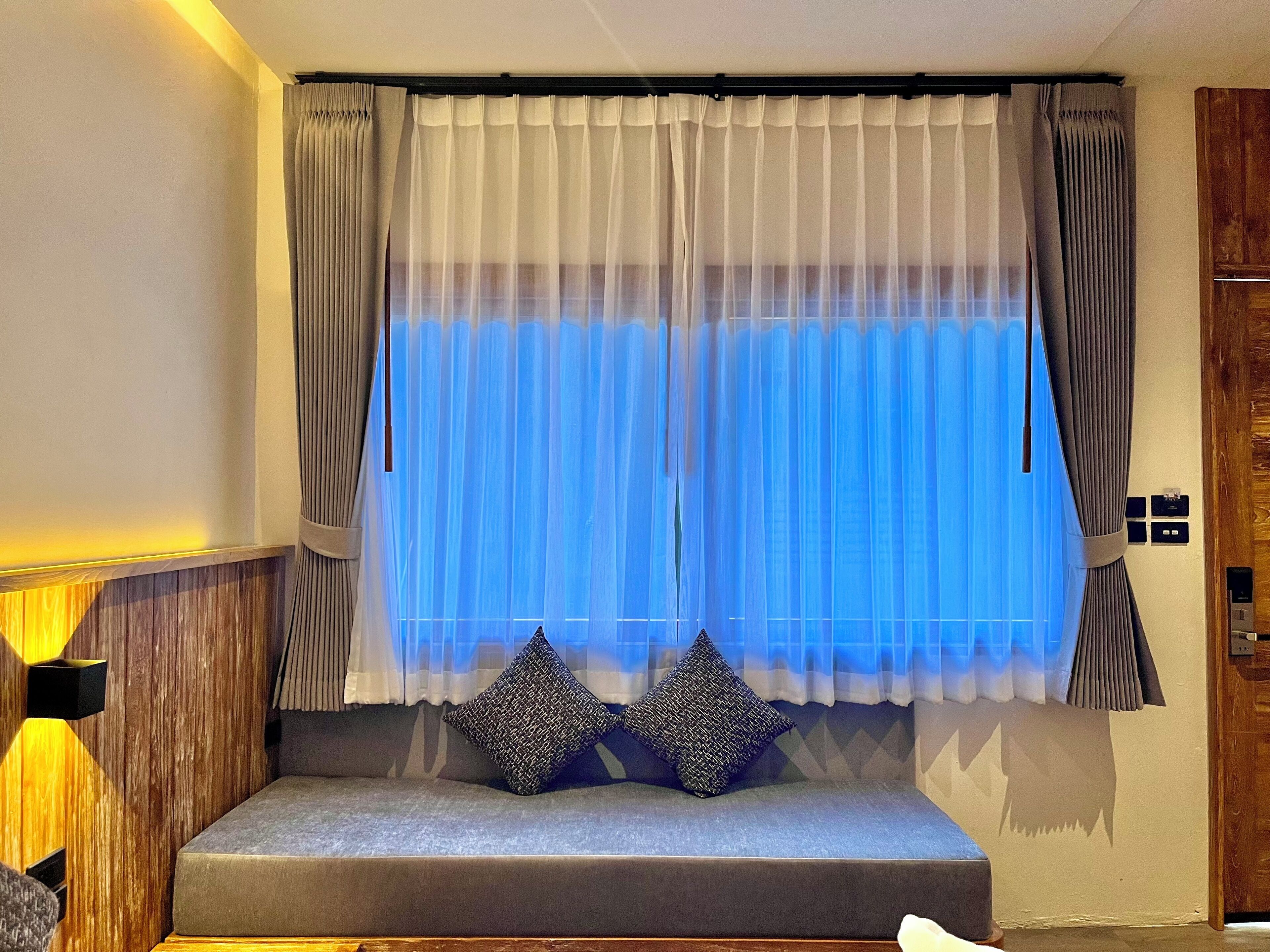 A room with a large window, a sofa with two pillows, and a wooden cabinet.