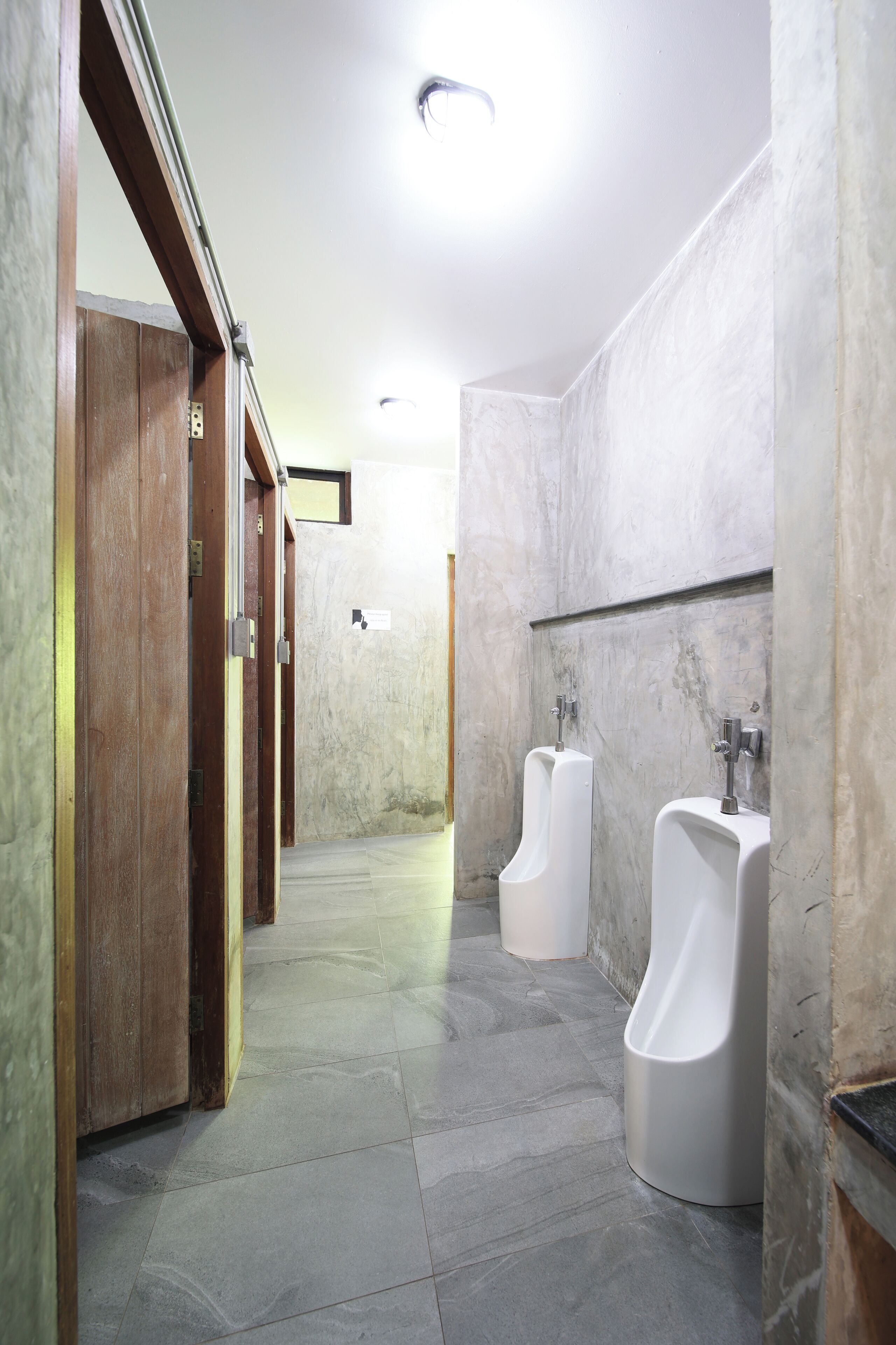 A modern restroom with marble walls, wooden doors, and two urinals.