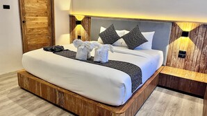 A modern hotel room with a wooden headboard, a large bed with white linens, two bedside tables with lamps, and a wooden floor. - The Chic Lipe - Hostel (Koh Lipe)