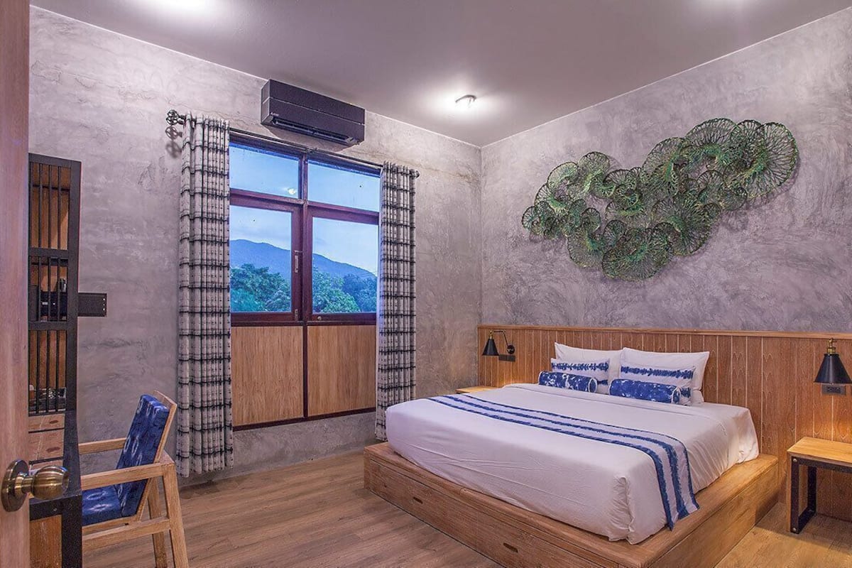 A bedroom with a bed, a window, a wall art piece, and a chair.