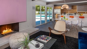 Een moderne woonkamer met een open haard, uitzicht op een zwembad en een keukenhoek.