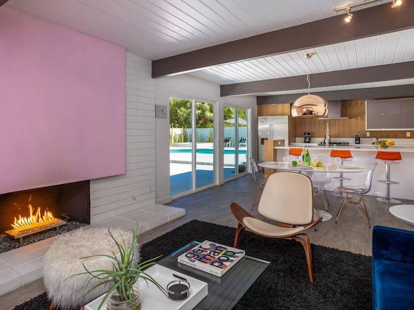Un salon moderne avec une cheminée, une vue sur la piscine et un coin cuisine.