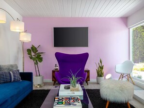 Ein modernes Wohnzimmer mit einem violetten Sessel, einem blauen Sofa, einem Couchtisch mit Zeitschriften und einem großen Fenster.