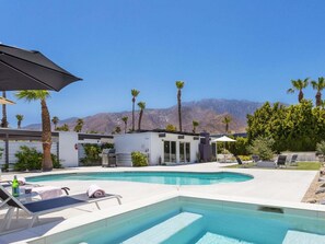 Un espace piscine moderne avec des chaises longues, un barbecue et une vue sur les montagnes.