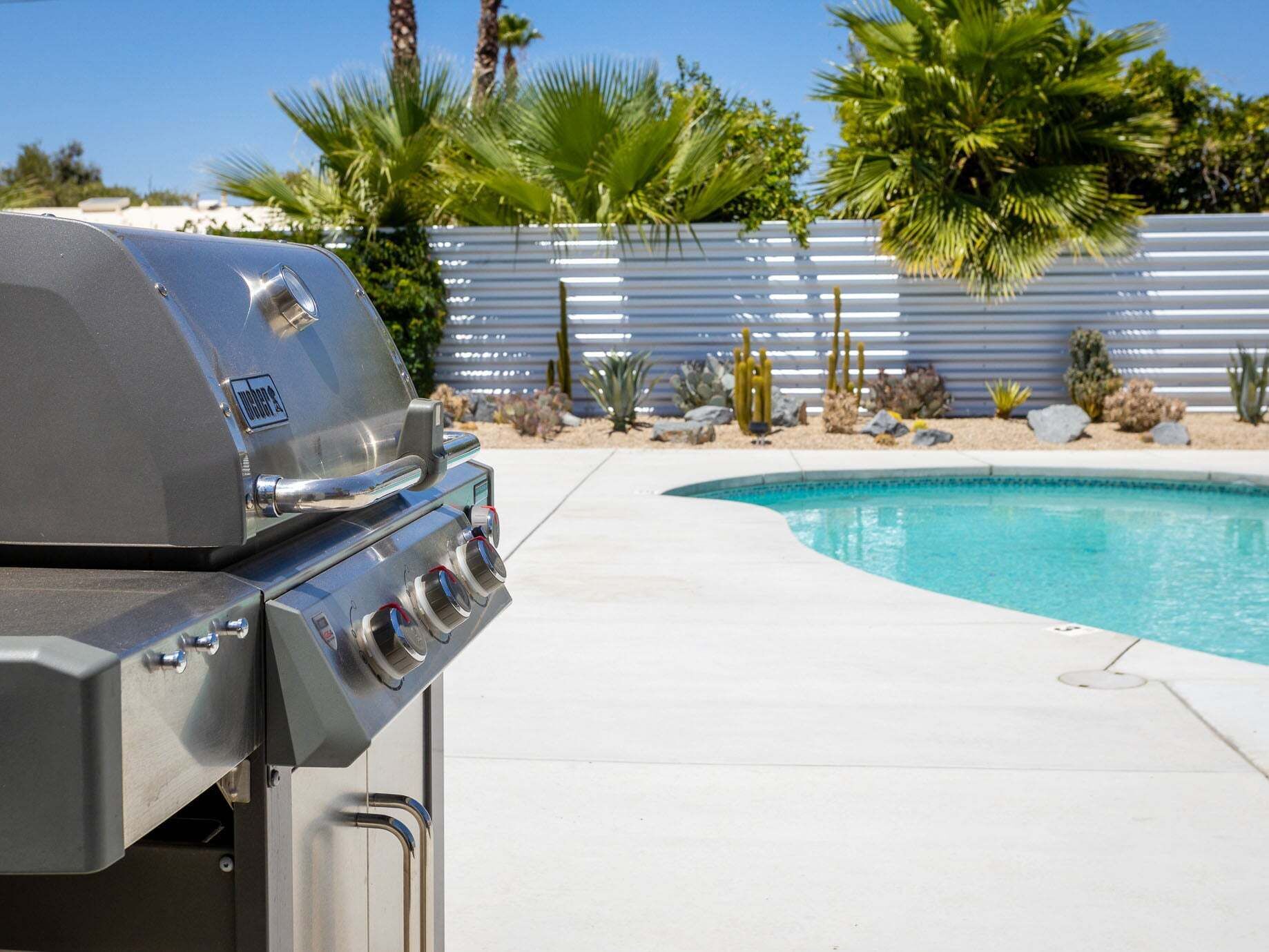 Una parrilla cerca de una piscina con un jardín desértico al fondo.