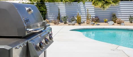 A barbecue grill near a swimming pool with a desert garden in the background.