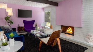 Een moderne woonkamer met een open haard, een flatscreen televisie en een paarse fauteuil.