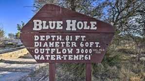 A wooden sign with text describing Blue Hole's depth, diameter, outflow, and water temperature.