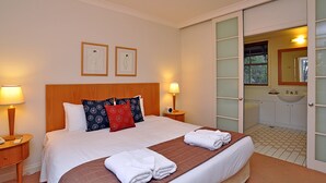 Une chambre d’hôtel comprenant un lit, deux lampes de chevet, une table de chevet, un grand miroir et une salle de bain avec un lavabo et des toilettes.