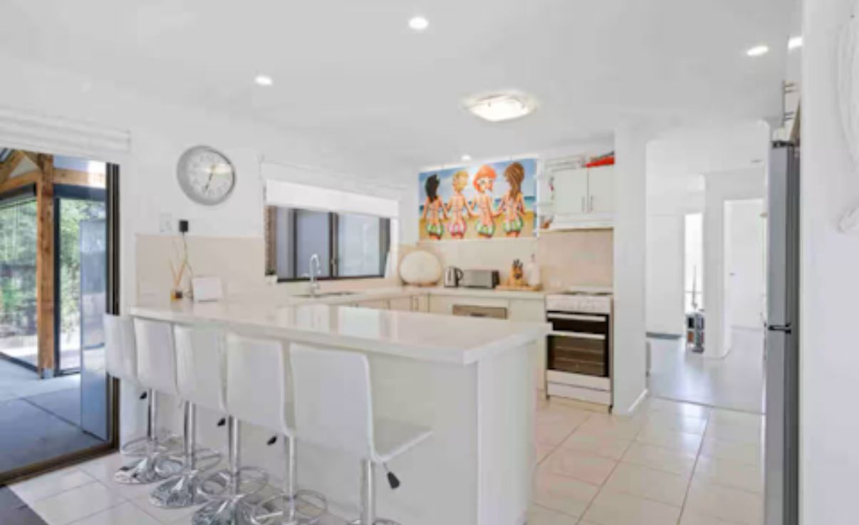 Een moderne keuken met een centraal eiland, barstoelen en een groot raam.