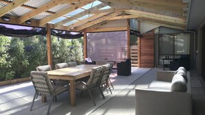 An outdoor patio with a wooden table and chairs, a barbecue grill, and a covered seating area. - Beach House Getaway #2 (Smiths Beach)
