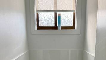Ein kleines, sauberes Badezimmer mit Toilette, Toilettenpapier, Mülleimer und einem Fenster über der Toilette.