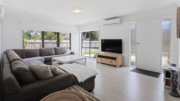 A modern living room with a sectional sofa, a coffee table, and a TV on a wooden stand. - Beach House Getaway #2 (Smiths Beach)