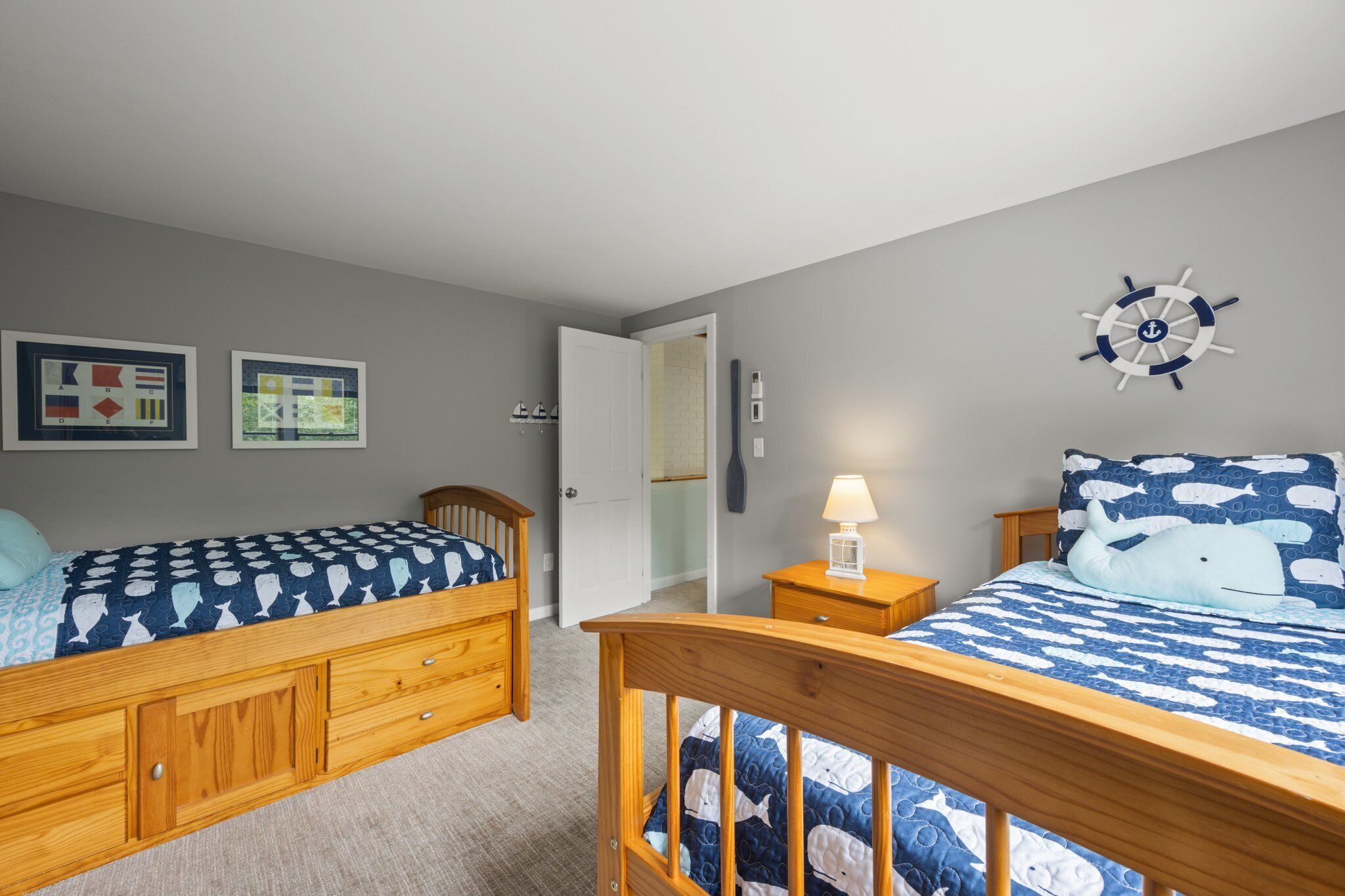 A bedroom with two beds, wooden headboards, a wall clock, and a door leading to another room.