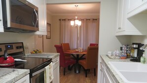 A compact kitchen with a microwave, oven, and a coffee maker. There is a dining table with chairs and a chandelier above. - Have a "Hakuna Matata" apline vacation in Style & Luxury!! (Helen)