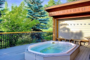 A hot tub on a wooden deck with a railing, surrounded by trees.
