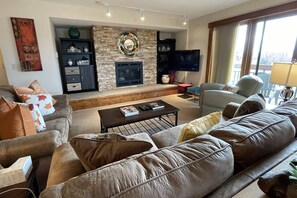 A living room with a stone fireplace, a flat-screen TV, a sofa, and a chair. - Hike Out/Walk In w/Unforgettable Views-Hot Tub-Garage-Grill-Deck-W/D in Unit-Fireplace-Updated/Quiet (Steamboat Springs)