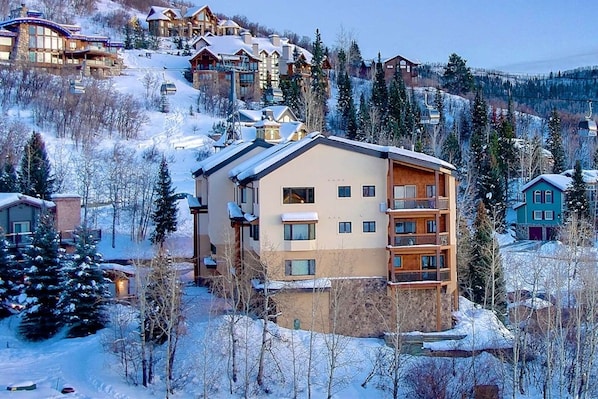 A multi-story hotel with a ski lift in the background, surrounded by snow-covered trees and buildings.