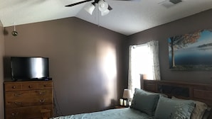Een slaapkamer met een bed, een dressoir, een plafondventilator en een schilderij aan de muur.