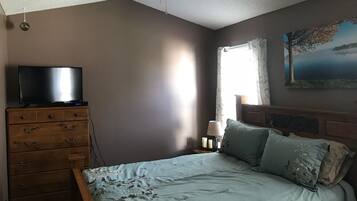 Une chambre à coucher avec un lit, une commode, un ventilateur de plafond et un tableau accroché au mur.