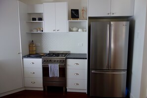 A kitchen with white cabinets, a stainless steel refrigerator, a gas stove, and a small wooden shelf with a 'HELLO' sign. - The Lighthouse (East Toowoomba)