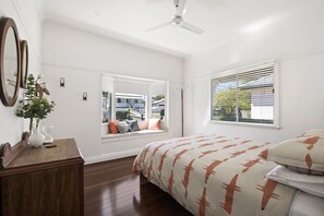 Un dormitorio con cama, un rincón con asiento junto a la ventana, ventilador de techo y vistas al exterior.