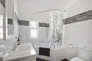 A modern bathroom with a white sink, a bathtub, and a shower curtain with a tree design. - The Lighthouse (East Toowoomba)