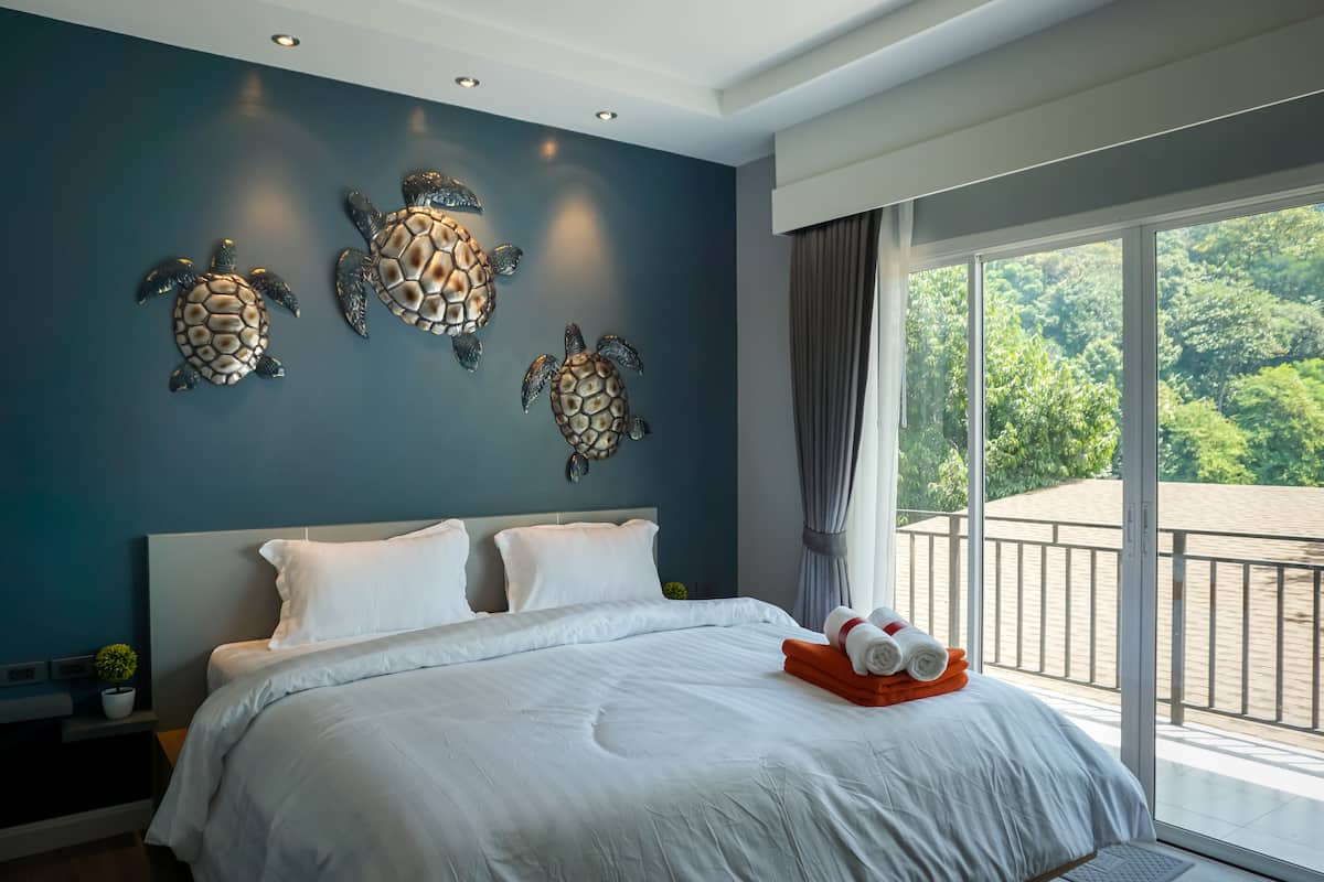 Quarto com cama grande, varanda com vista para vegetação e arte decorativa de tartarugas na parede.