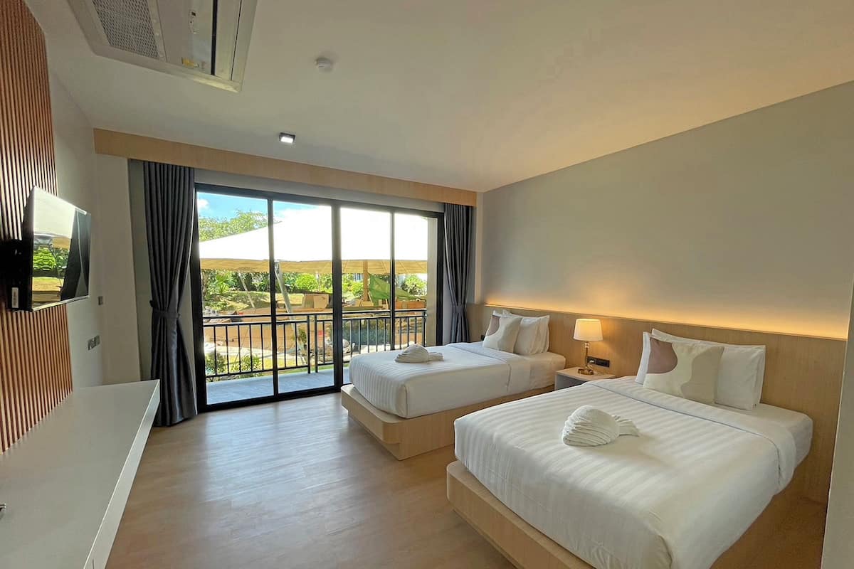 Quarto de hotel com duas camas, televisão e varanda com vista para o exterior.
