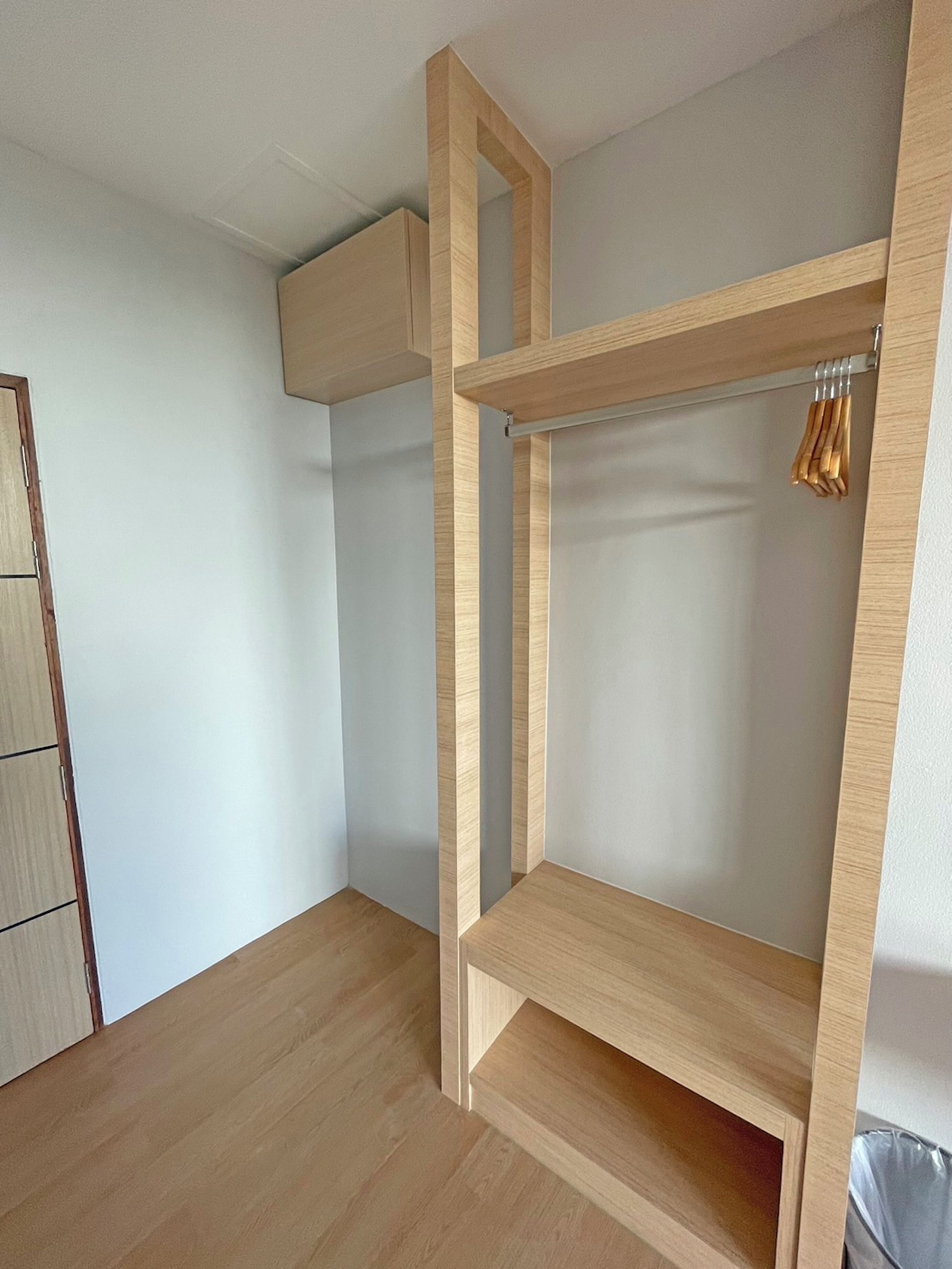 Una habitación con un armario de madera, barra para colgar ropa y un cubo de basura.