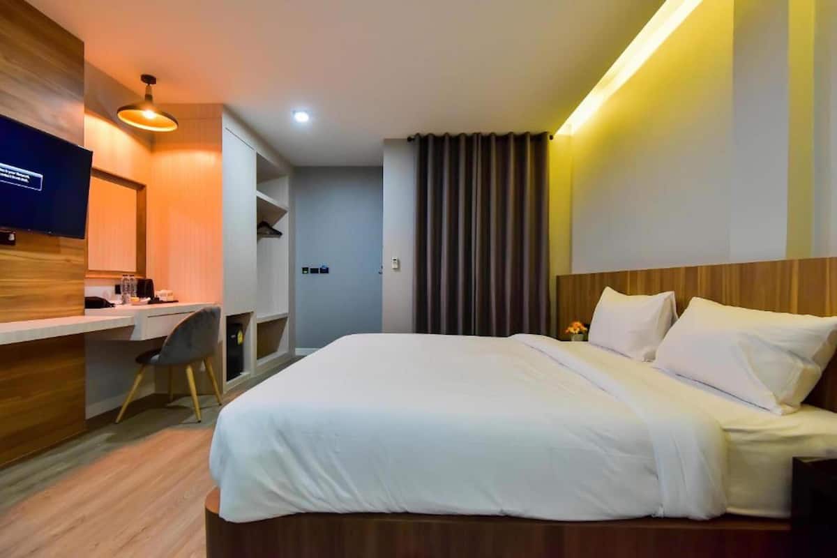 Quarto de hotel com uma cama grande, uma escrivaninha com cadeira, televisão e cortina.