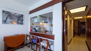 A compact kitchen with a microwave, stove, and sink. There are three wooden chairs with cushions. A wooden table is positioned in front of the kitchen. - Direct & Private beach access. 30 km from Lisbon (Sesimbra)