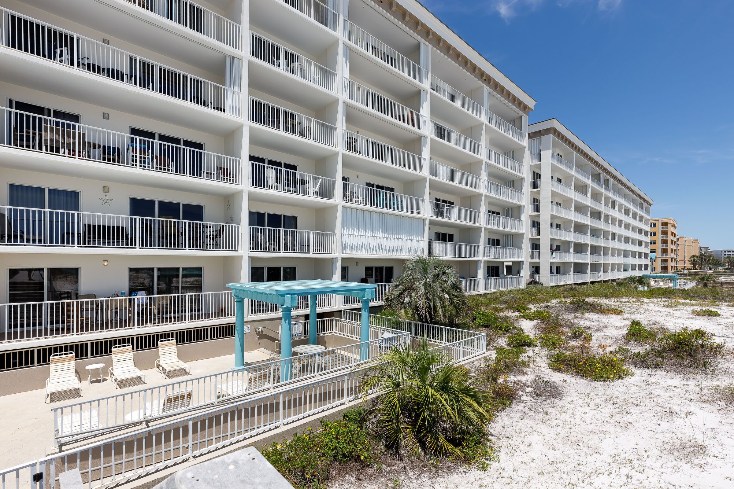 A multi-story hotel with balconies, outdoor seating, and a beach view.