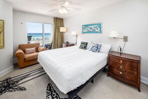 Une chambre à coucher avec un lit, une commode, une chaise, un ventilateur de plafond et une vue sur la plage.