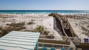A beach with a wooden walkway leading to the water, a sandy area with beach chairs, and a sign indicating pool rules.