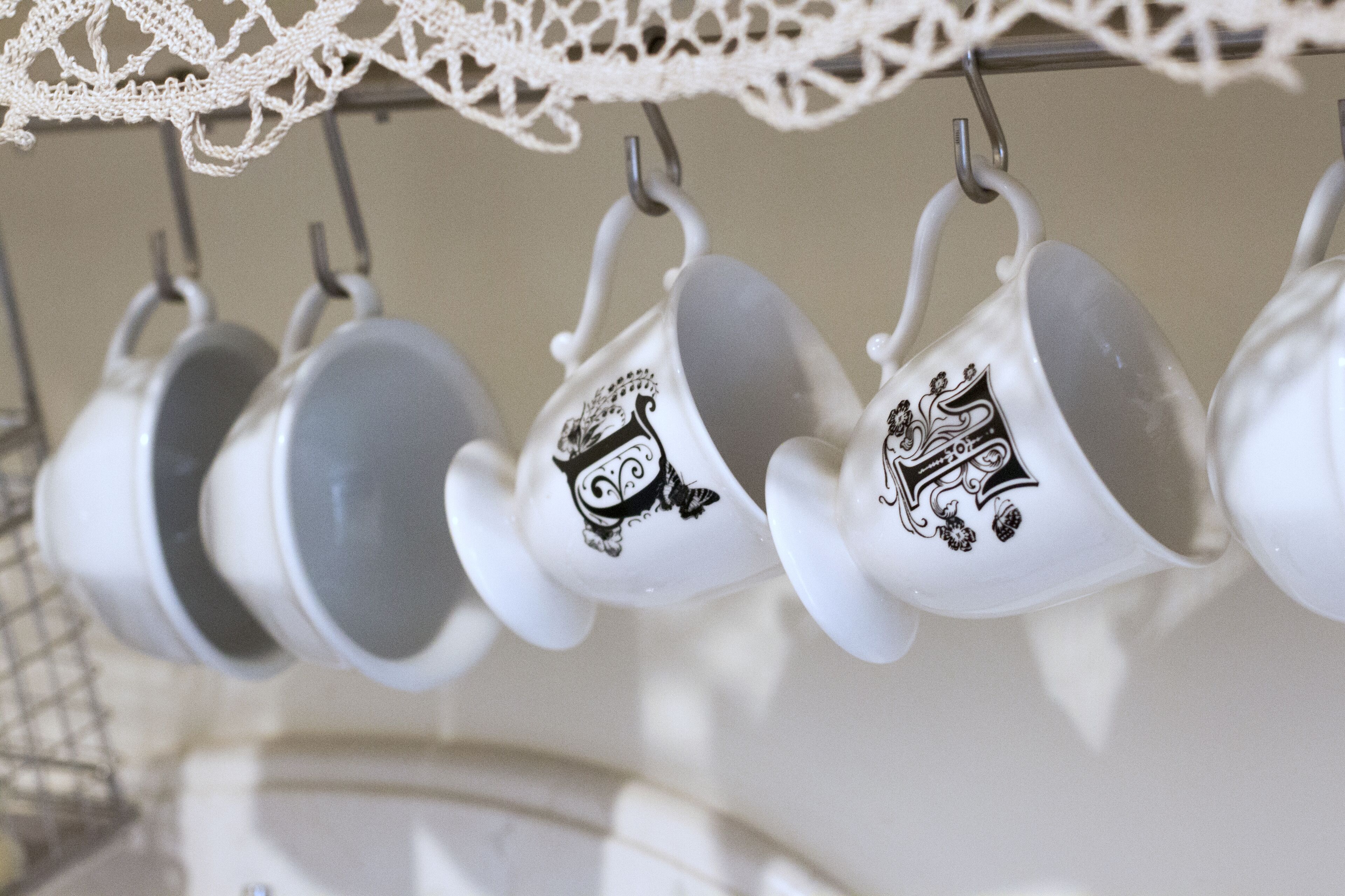 A rack of white ceramic cups with black designs, hanging from a metal hook.