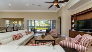 A spacious living room with a white sofa, striped armchairs, a coffee table, and a large flat-screen TV. - Private Pool | Single Floor Home | Near Attractions (Kissimmee)