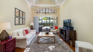 A spacious living room with a white sofa, a coffee table, a TV, and a fireplace. - Private Pool | Single Floor Home | Near Attractions (Kissimmee)