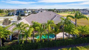 A residential area with a large house featuring a tiled roof, a swimming pool, and palm trees. - Private Pool | Single Floor Home | Near Attractions (Kissimmee)