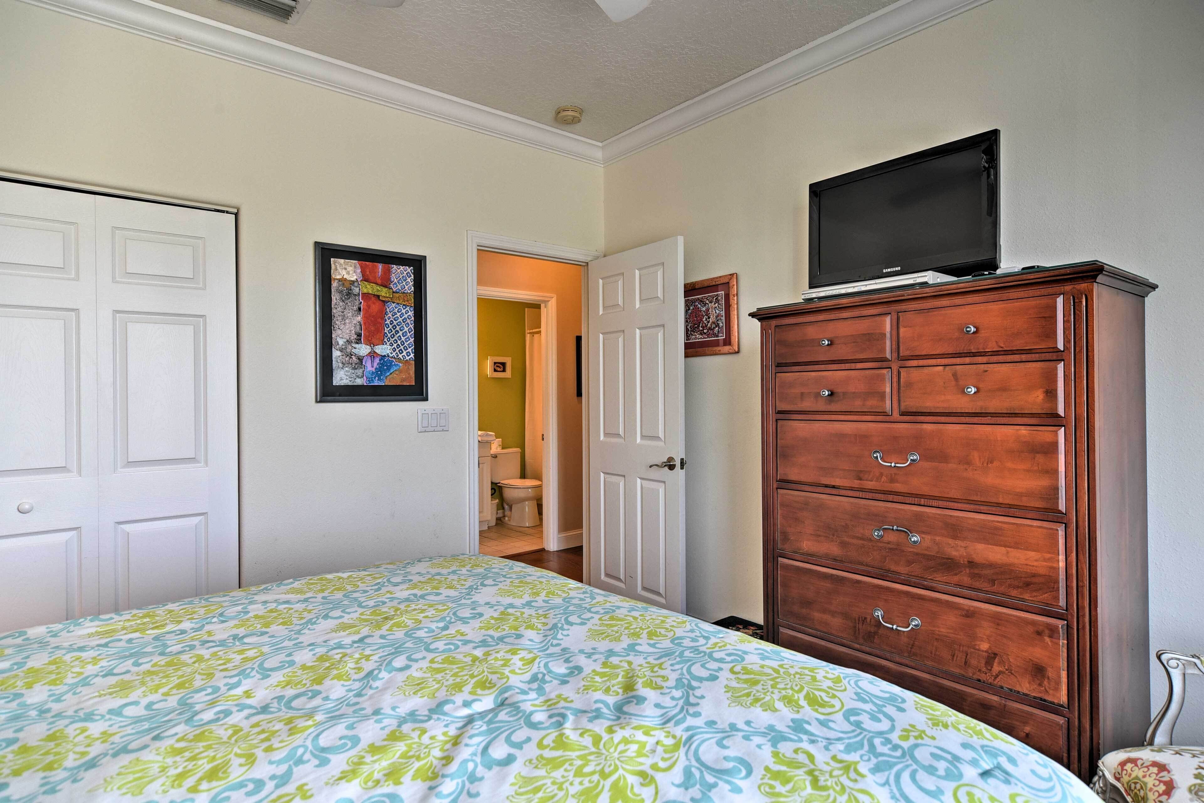 A bedroom with a bed, a dresser, a television on top of the dresser, and a door leading to a bathroom.