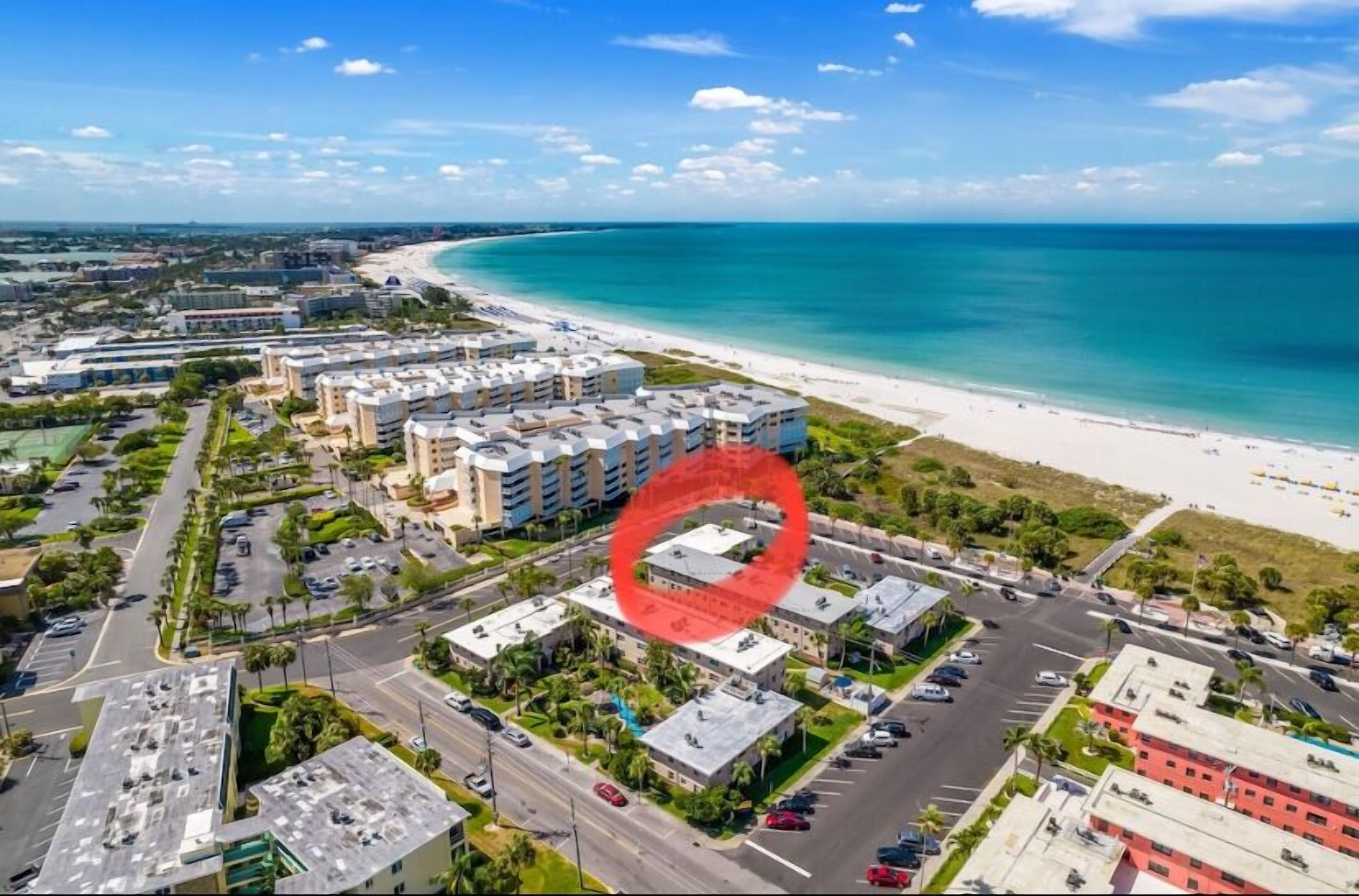 Vista aèria d'una zona costanera amb una platja, un aparcament i diversos edificis.