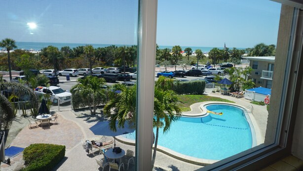 Vista de una piscina de diseño curvo, rodeada de palmeras y un estacionamiento con varios coches.