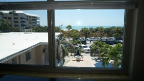 Vista desde una ventana sobre un estacionamiento con varios coches, un pequeño área de estar al aire libre y un edificio al fondo.