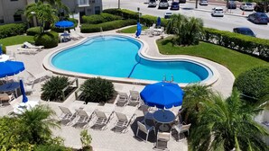 A swimming pool with lounge chairs and umbrellas, surrounded by greenery and a parking area with cars. - Beach views, poolside, new kitchen,  2 BR beach condo, KING bed ~ FN 304 (St Pete Beach)